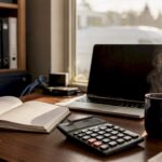 Desk with calculator, ledger, and laptop in office